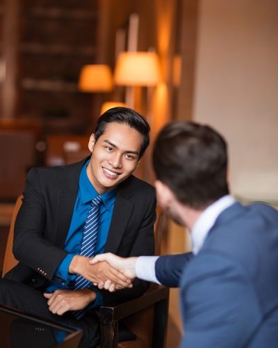 Closeup of two smiling business men shaking hands in cafe. One man is sitting back to camera.